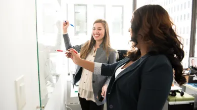 Two women in an office writing on a whiteboard