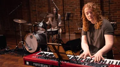Two young musicians perform at the Turner Sims concert hall. The person in the foreground plays the keyboards, the person behind plays the drums.