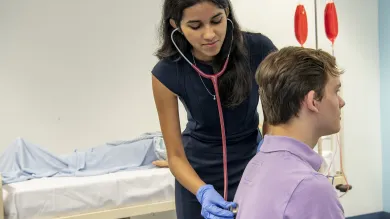 An undergraduate medicine student practices using a stethoscope on a patient in the clinical skills suite