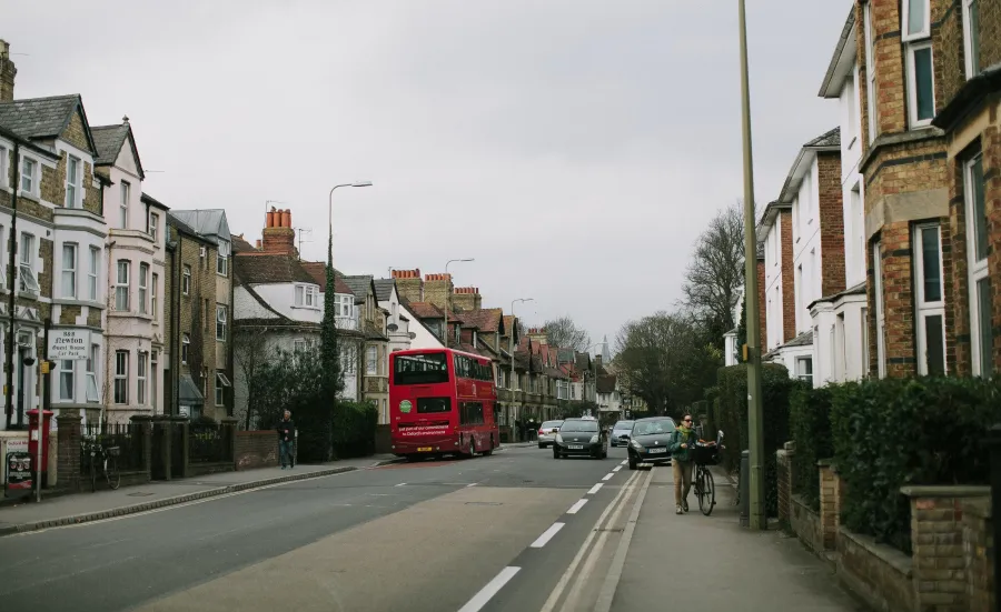 A road with a red bus, a cyclist pushing a bike, a pedestrian and cars