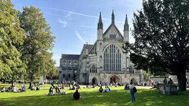 Exterior of Winchester cathedral with several people sat in the surrounding grounds.