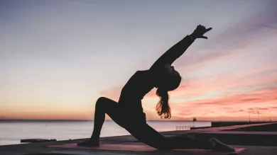 Silhouette of a person doing yoga by the water at sunset.