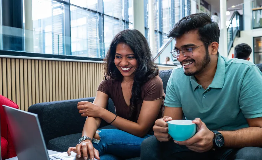 Two students huddle around a laptop together checking information on the screen.