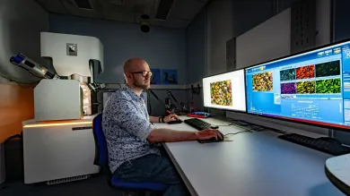 A technician works at computers displaying microscopic images, with a TESCAN electron microscope nearby.
