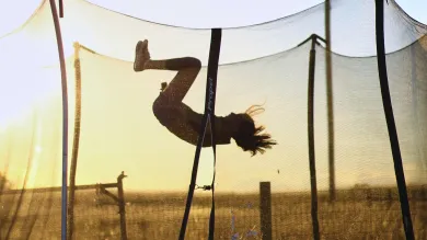 Child performing a flip on a trampoline during sunset in a field.