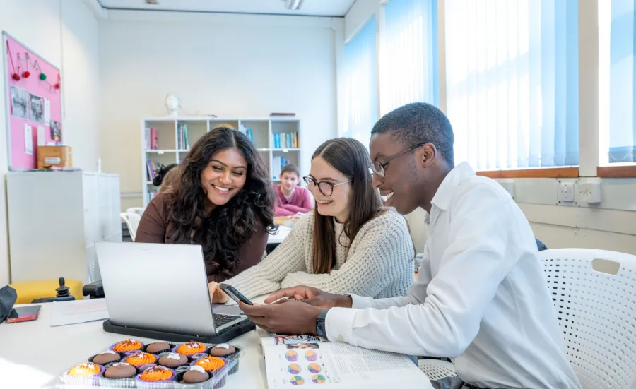 Students smiling looking at a laptop in a classroom.