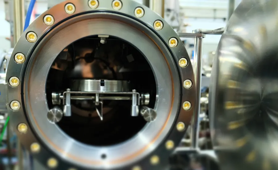 large, cylindrical metal chamber, likely part of scientific or industrial equipment. The chamber is open, revealing a complex mechanism inside. 