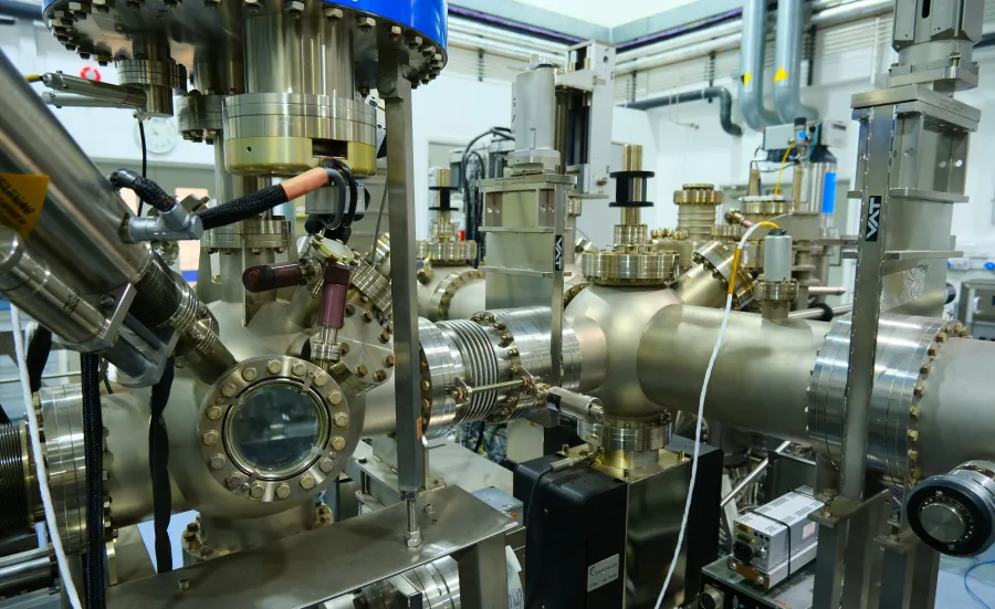 complex assembly of industrial machinery, likely a component of a laboratory or manufacturing facility. The machinery is composed of shiny metal parts, including cylindrical and conical segments connected with various flanges and bolts.