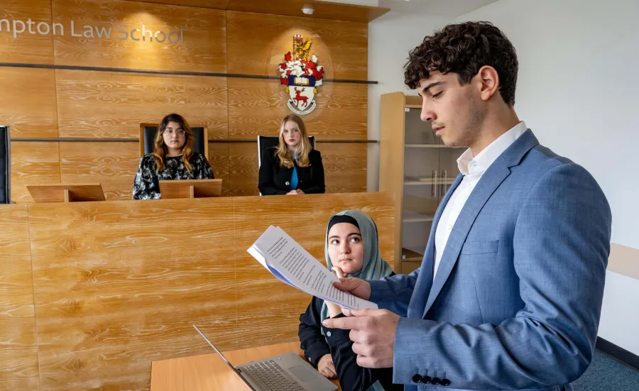 Law students participate in a mock trial, with a student presenting a case before a panel in a university moot court.