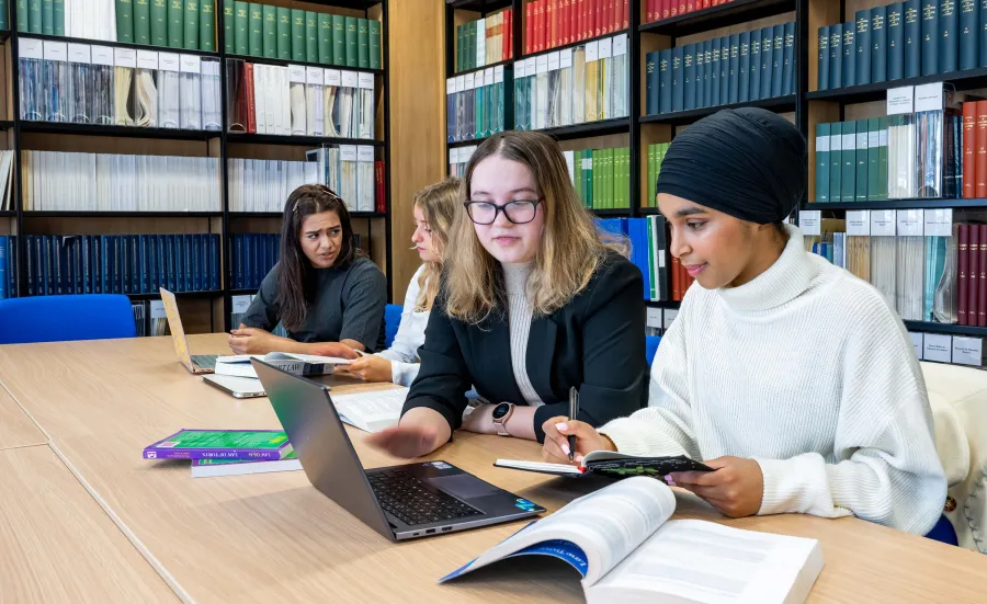 Four law students study together at a library table with laptops and open textbooks.