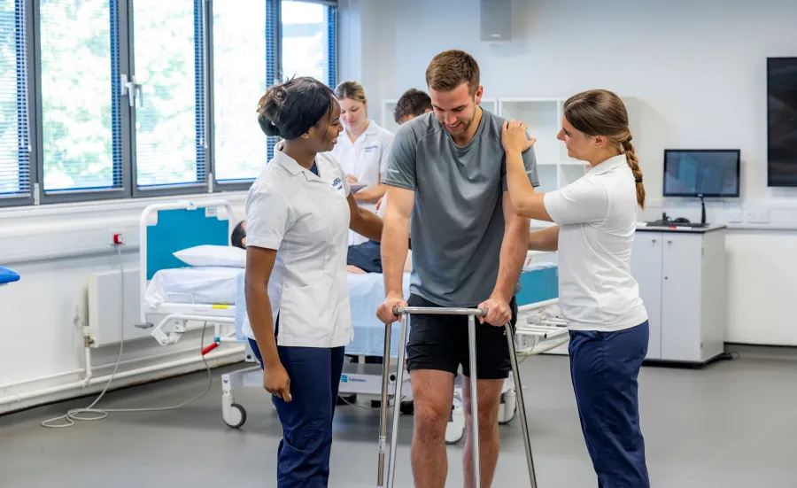 A patient, supported by 2 students, learns to walk using a walking frame.