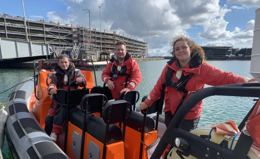 Three instructors standing on a powerboat moored at the quay side. They are all and looking directly at the camera. You can see the multistorey cruise parking building in the background.