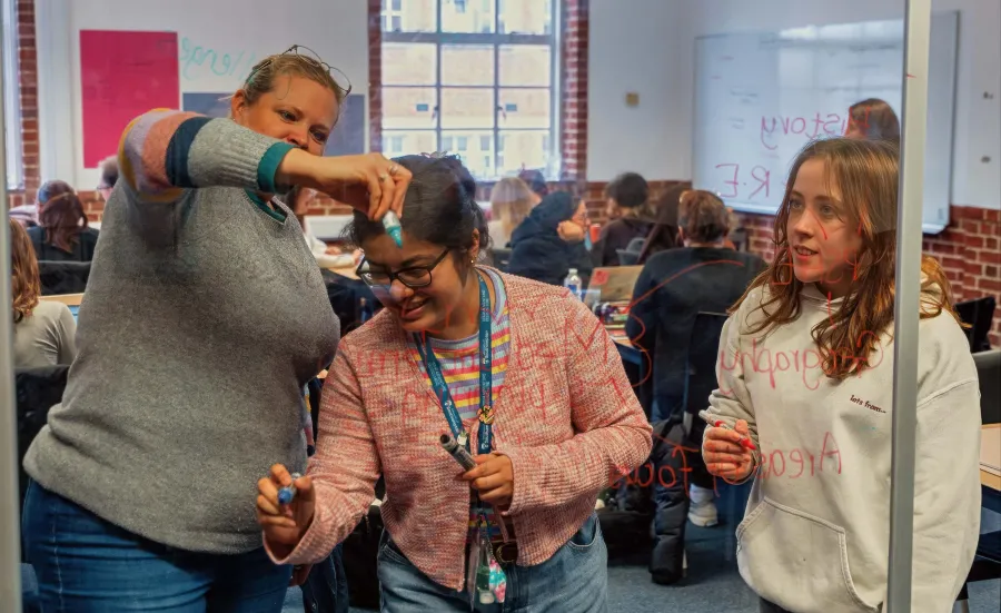 Students collaborating in class, writing on a transparent board.