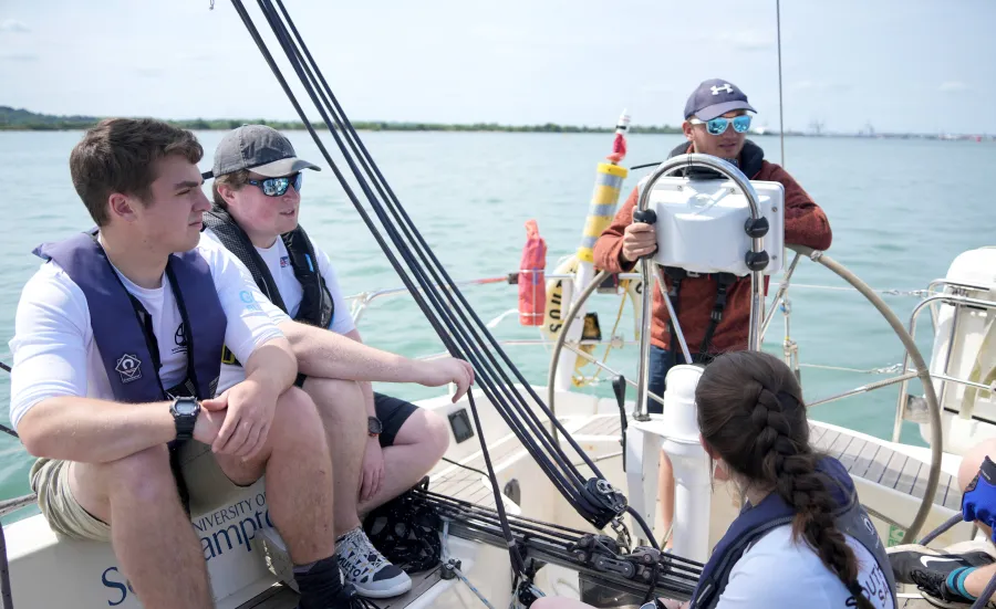 Students sitting on a boat, watching an instructor.