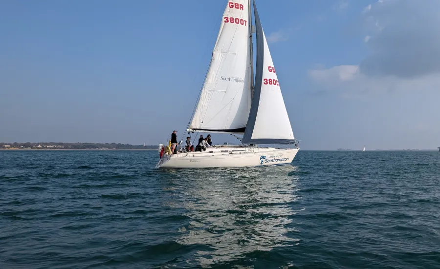 A yacht with 2 sails up and course participants sailing along the coast
