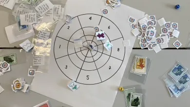 A tabletop game in progress showing cards, tokens and a target board used for exploring character, emotion and decision-making.