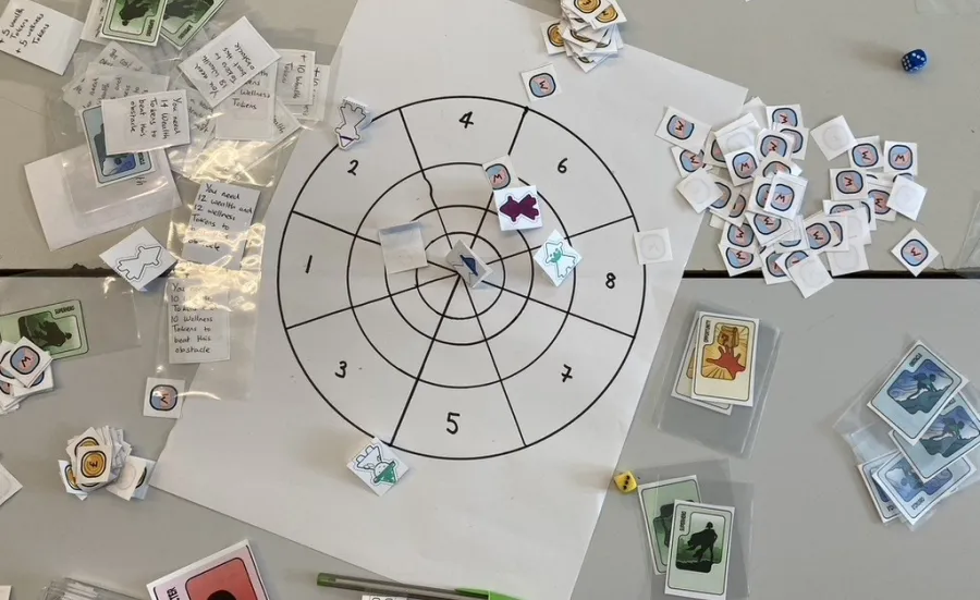 A tabletop game in progress showing cards, tokens and a target board used for exploring character, emotion and decision-making.
