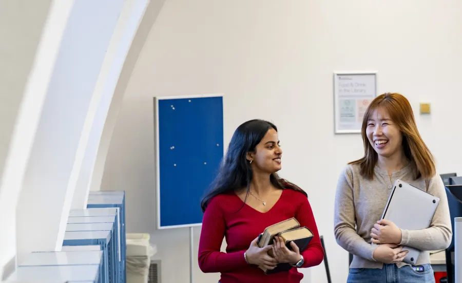 Two English literacy students talking and smiling as they walk through a room in the library set up with computer workstations. 