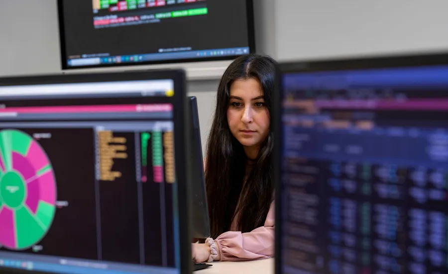A student is surrounded by Bloomberg terminals, showing data in various colourful representations. 