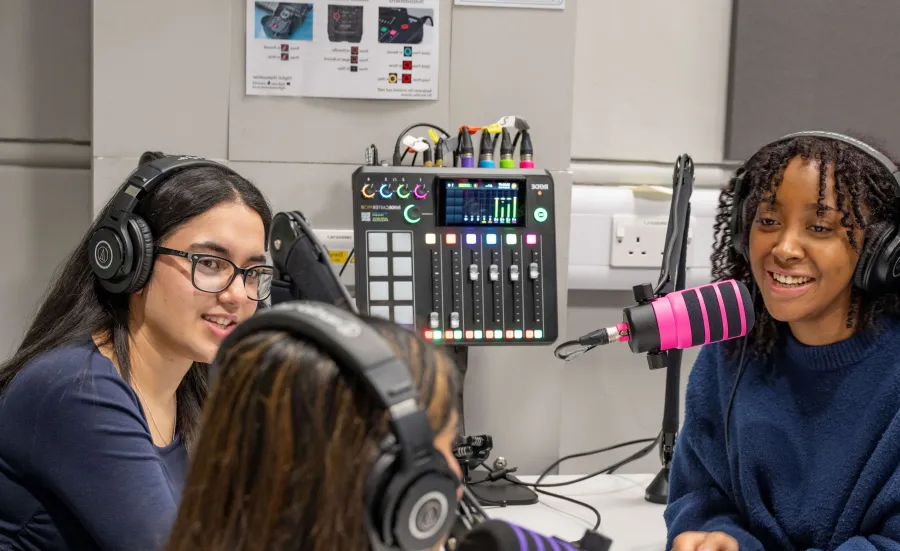 Three BA Film, TV and Digital Media students in a recording studio. All 3 students have headphones on and a large microphone in front of them.