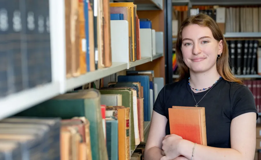 Joely Fake, global challenges - history student, holding a book in the library