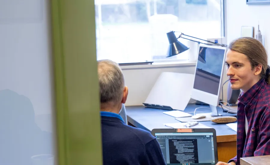 A philosophy student sitting with their tutor in an office. They are discussing work on a laptop. 