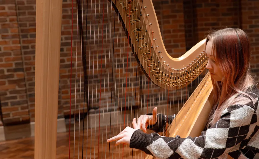 A student in the playing a harp in the Turner Sims hall.