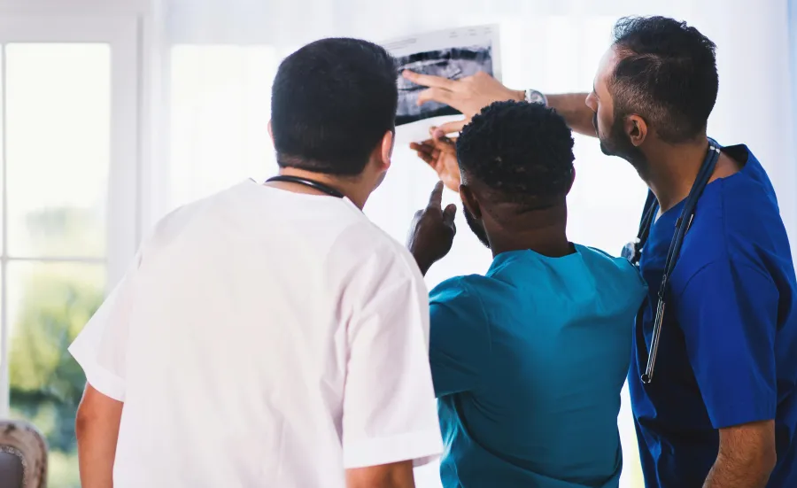Three healthcare professionals examining an X-ray next to a window.