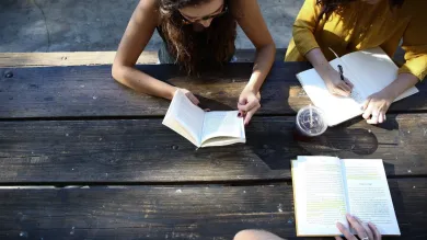 Three people gathered around at a picnic table while reading books and writing notes