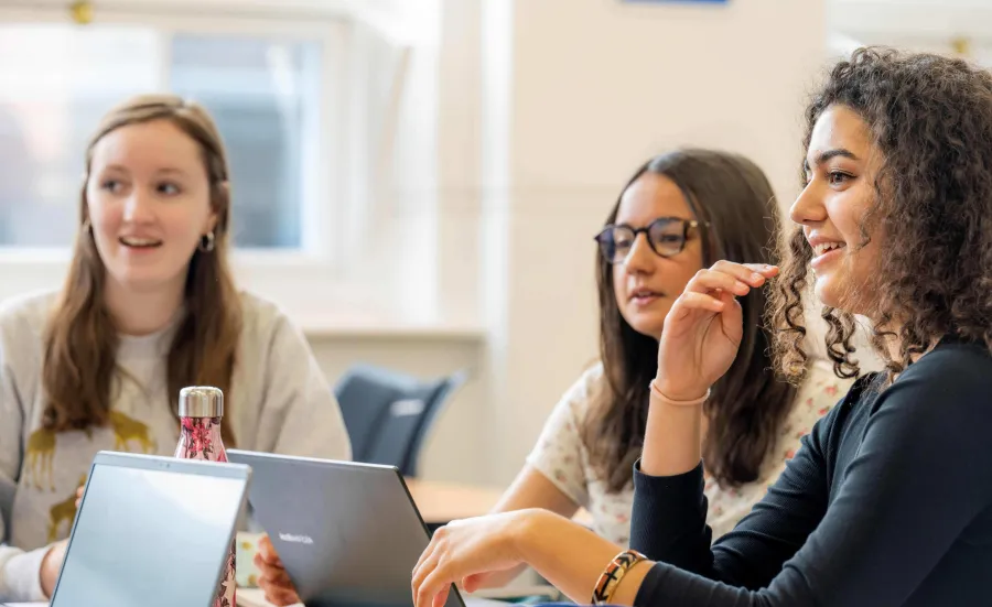 3 modern Languages students in a class. There are books and laptops open on the desk.