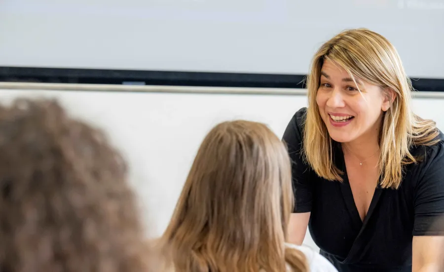 A modern languages tutor is smiling and looking at her class room of students.