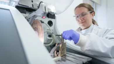 Person in a lab coat and goggles clamping sample at saw