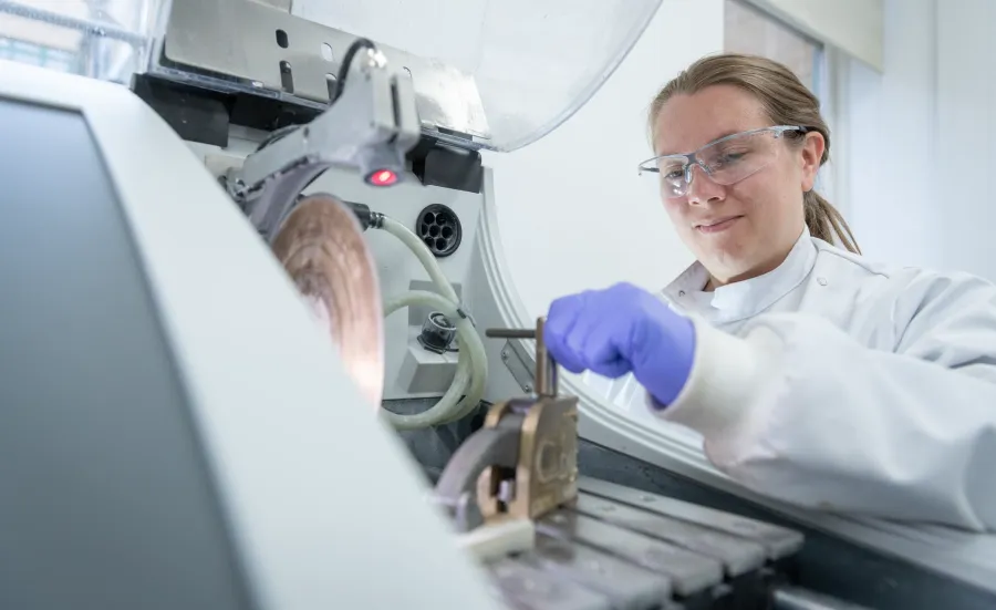 Person in a lab coat and goggles clamping sample at saw