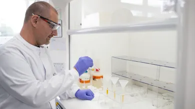 A person in a lab coat and gloves works in a laboratory