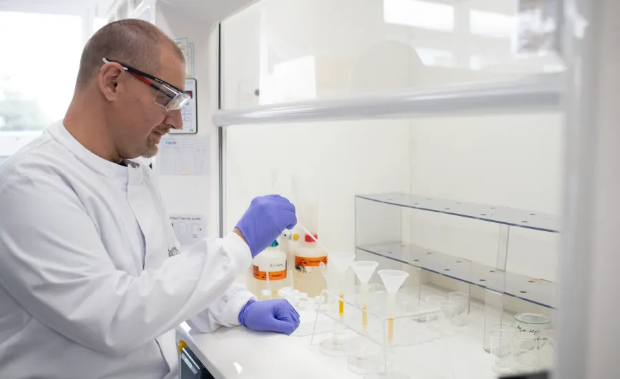 A person in a lab coat and gloves works in a laboratory