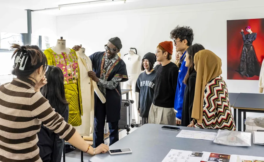 Fashion design tutor presenting a garment to a group of students in a studio.