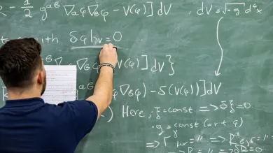 A student writing a mathematical equation on a blackboard, in a study and social space on a university campus.