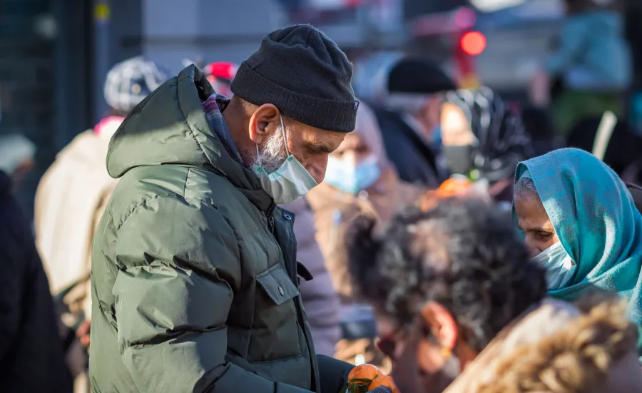People wearing masks gather outdoors, some handing out fruit during a community food distribution.