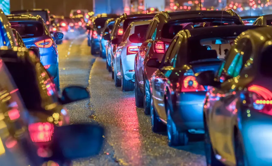 Looking along 2 rows of cars, bumper to tail with the rear lights shining. it is dark apart from the car lights.