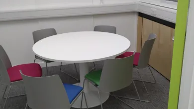 An empty meeting room with a round table surrounded by 6 plastic chairs.