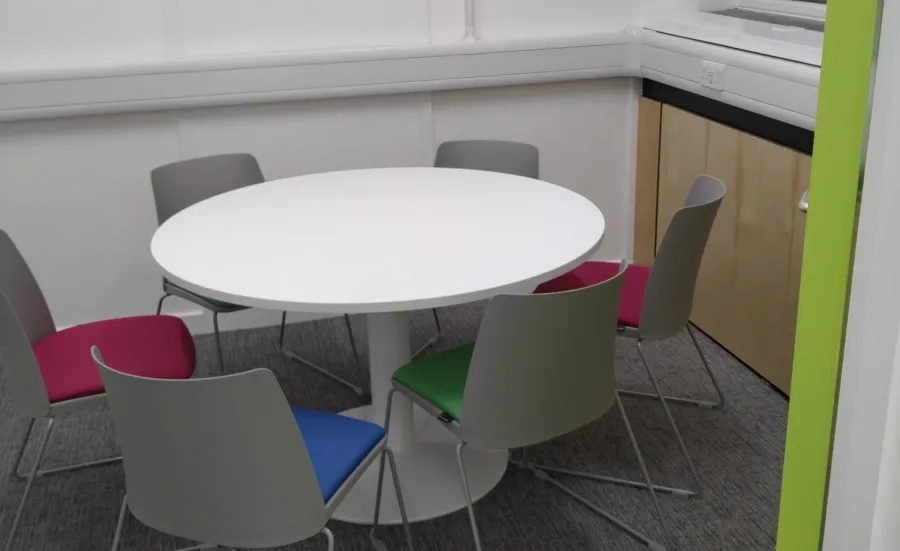 An empty meeting room with a round table surrounded by 6 plastic chairs.