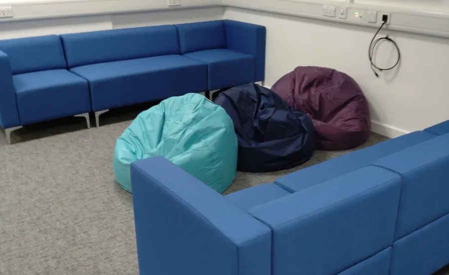 An empty room with sofas, beanbags, and a TV mounted on the wall.