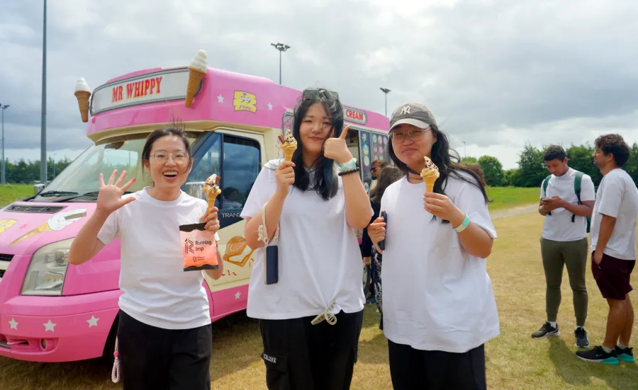 Three students stood holding ice creams, with an ice cream van in the background.