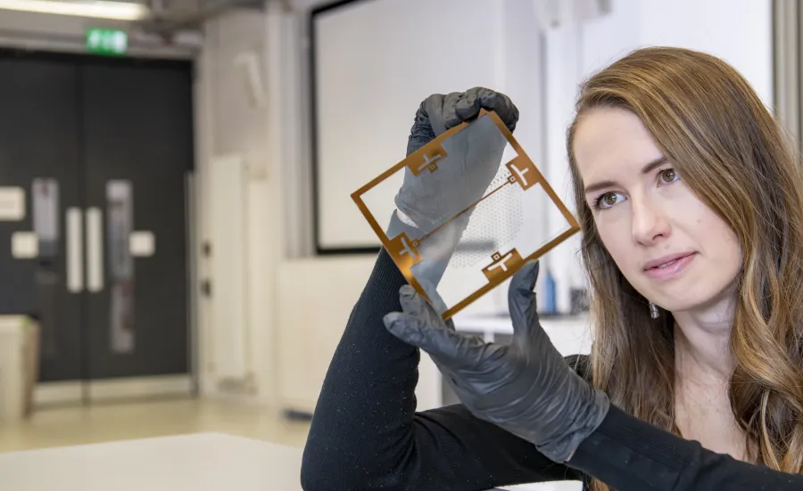 Person wearing gloves examines a transparent electronic component in a laboratory.