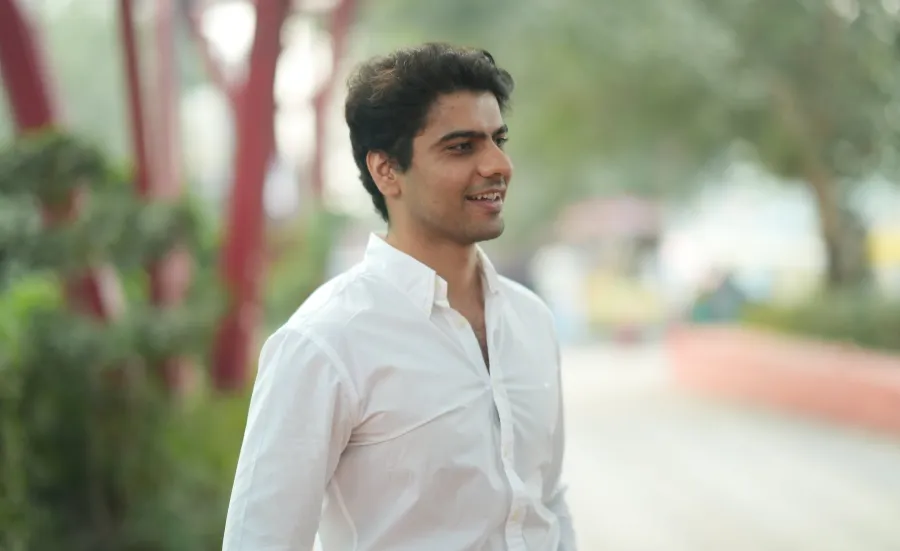 Law graduate and entrepreneur Rohit is standing looking to the right of the camera. There are out of focus trees and shrubs behind him.