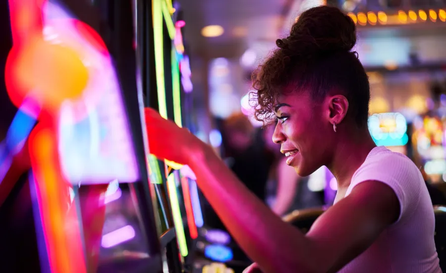 A woman playing a brightly lit slot machine in a casino.