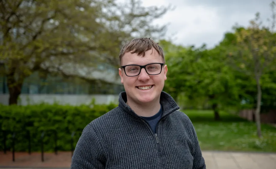 Smiling student wearing glasses standing outside the Physics building..