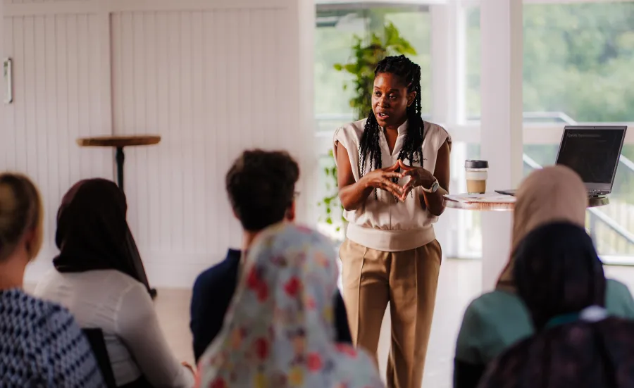 Monique, a Black Futures scholar, presents to an audience at a conference in a bright room.