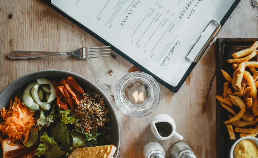 Table with a menu, bowl of salad and a plate of chips on it
