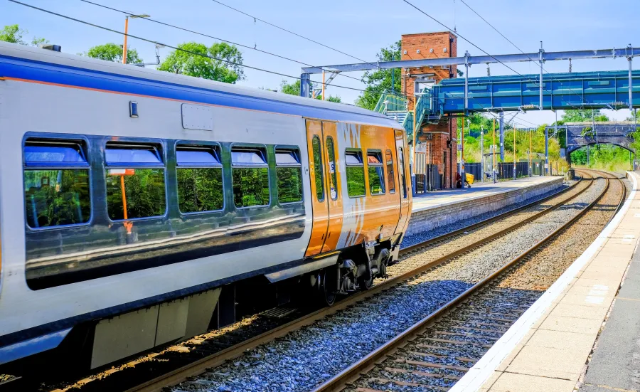 A modern passenger train pulling into a quiet railway station on a sunny day.